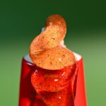 Close-up of Dzintars Asari Wild Strawberry Gel Toothpaste texture – translucent orange-red gel with green microbeads squeezed from the red tube