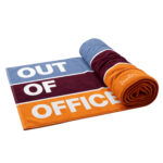 Dzintars Out Of Office premium cotton beach towel 90x170cm, 700 gsm – colour-block design in blue, burgundy and orange, partially rolled, white background