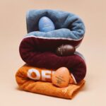 Dzintars Out Of Office beach towel rolled and stacked in three colour sections with Evenglow, Perfectglow SPF 30 and Amberglow SPF 50+ face balms nestled inside – summer skincare and beach essentials