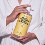 Person in white bathrobe holding Dzintars Sorry For Being Extra Gorgeous nourishing body cleanser 1000ml pump bottle